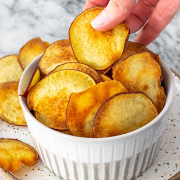 mão retirando um chips de batata-doce de um pote