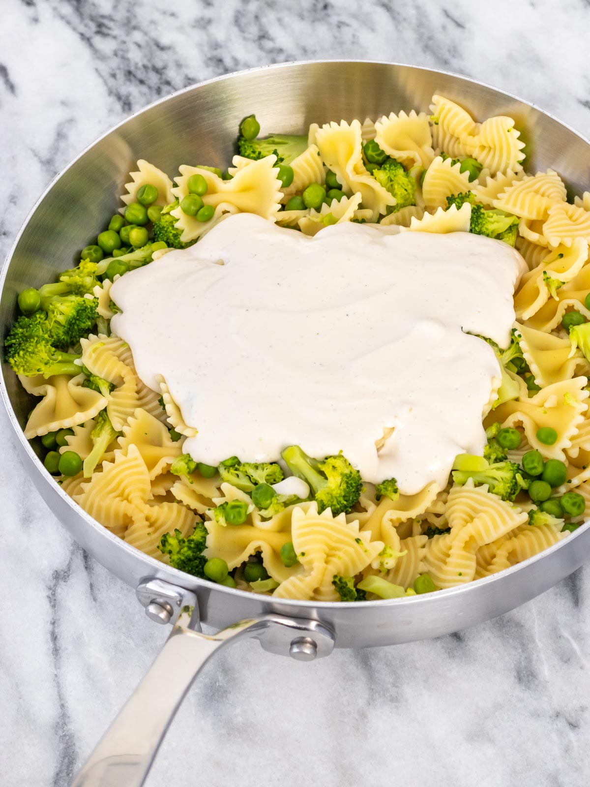 molho branco por cima do macarrão cozido com brócolis e ervilha