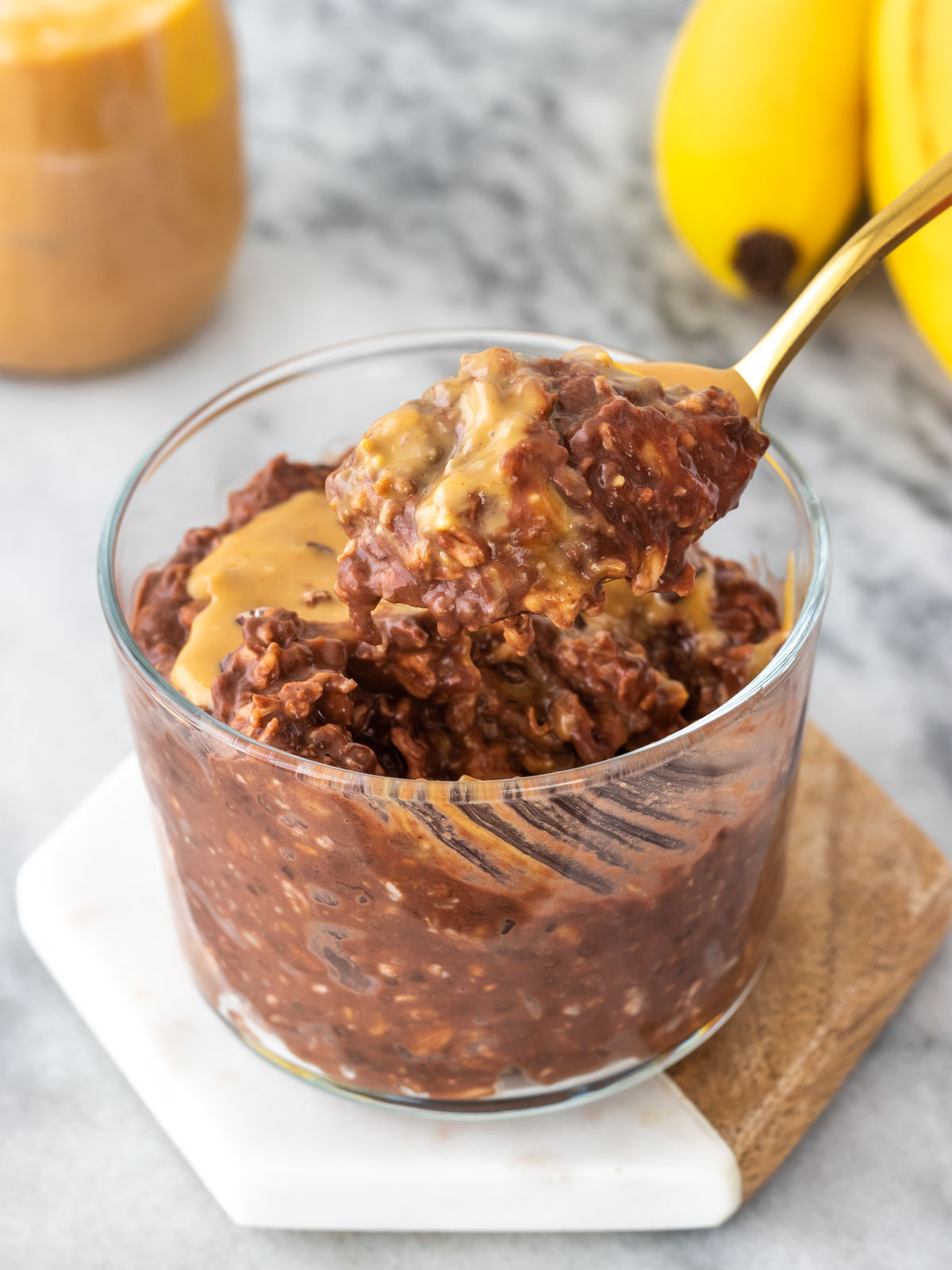 overnight oats de chocolate e banana servido em um copinho com pasta de amendoim e nibs de cacau