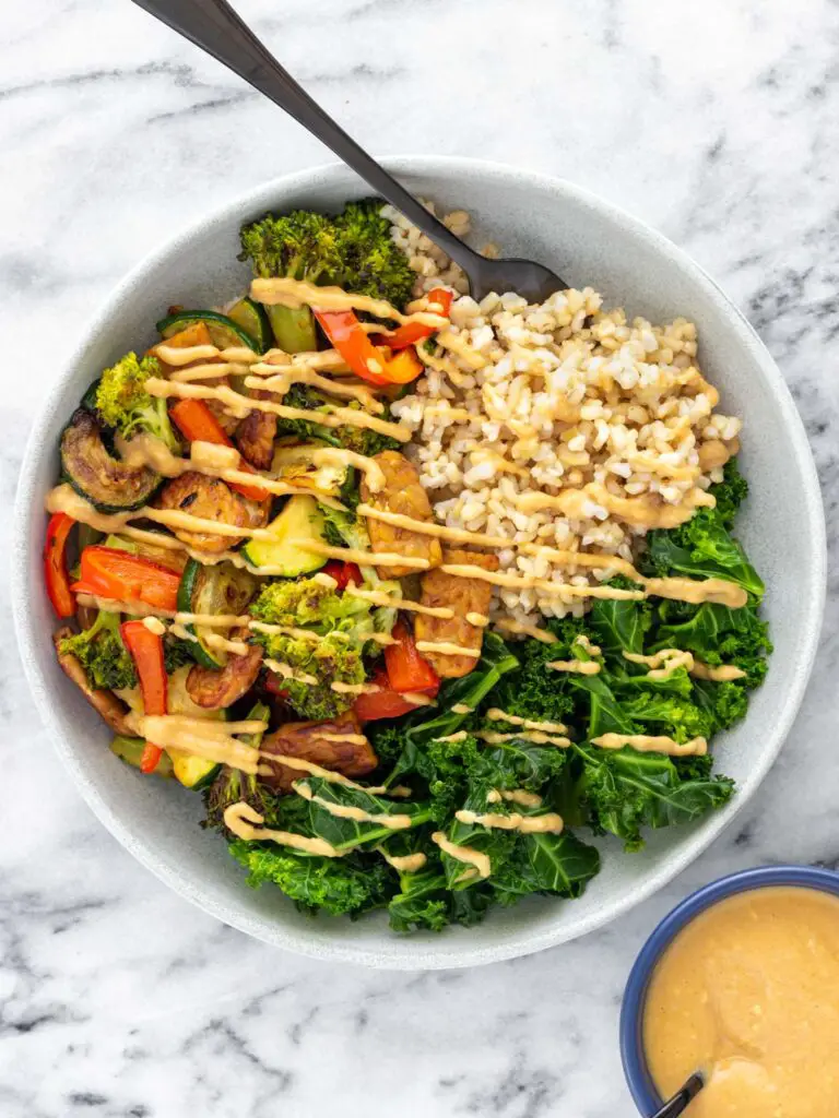 prato de comida com arroz integral, mexido de tempeh com vegetais, couve refogada e molho de missô com amendoim