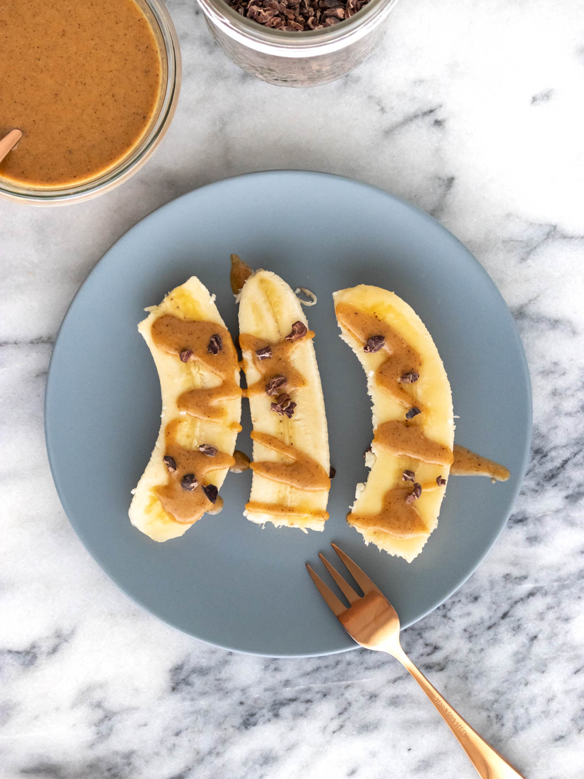 três fatiadas de banana servidas em um prato com pasta de castanha-do-pará e nibs de cacau