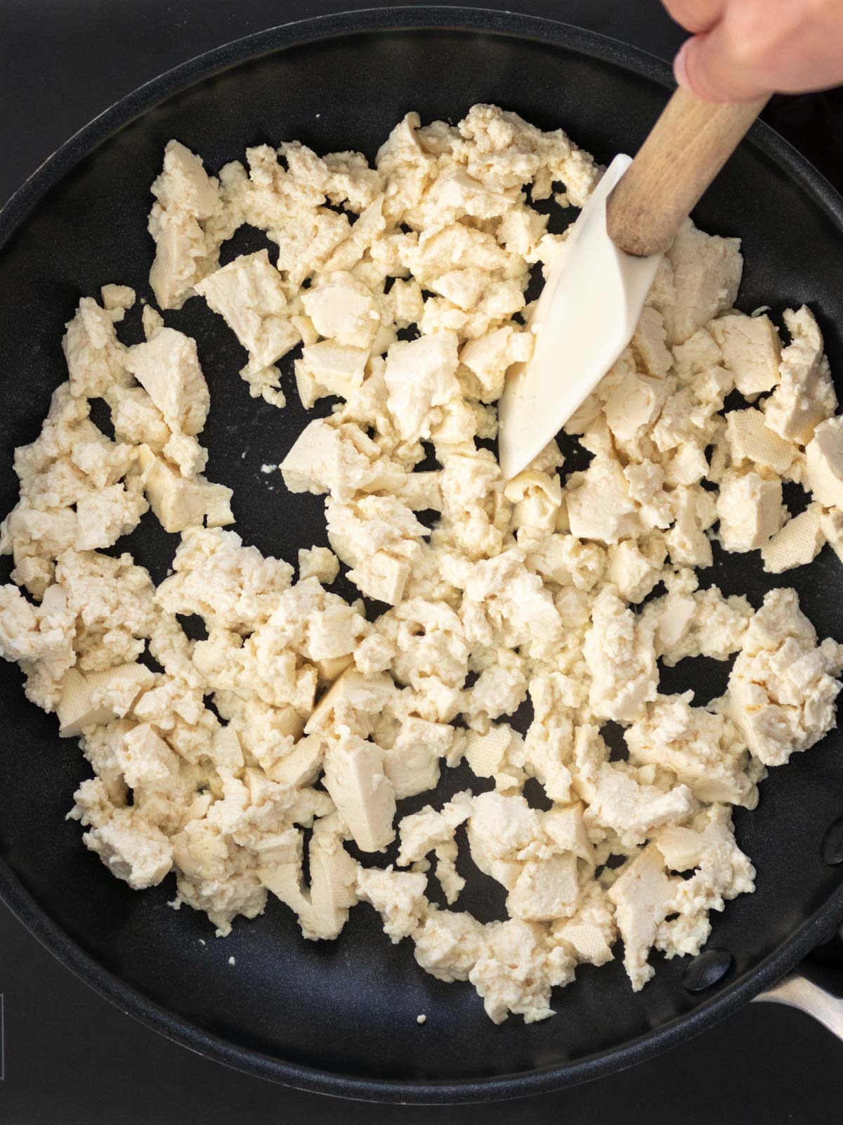 tofu quebrado em pedaços pequenos sendo refogado em uma frigideira