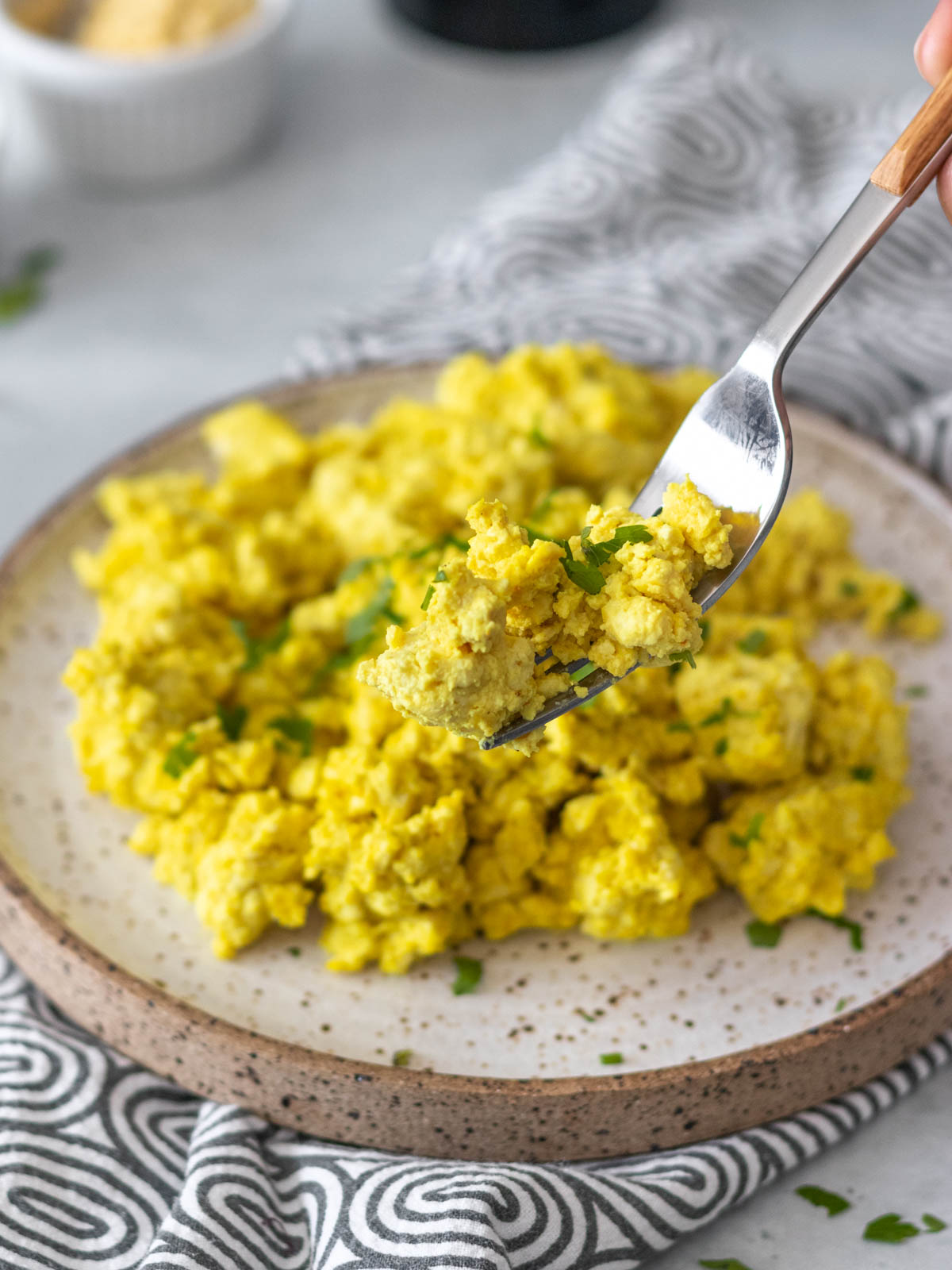 garfo com tofu mexido retirado de prato com mais tofu mexido cremoso servido com salsinha fresca picada