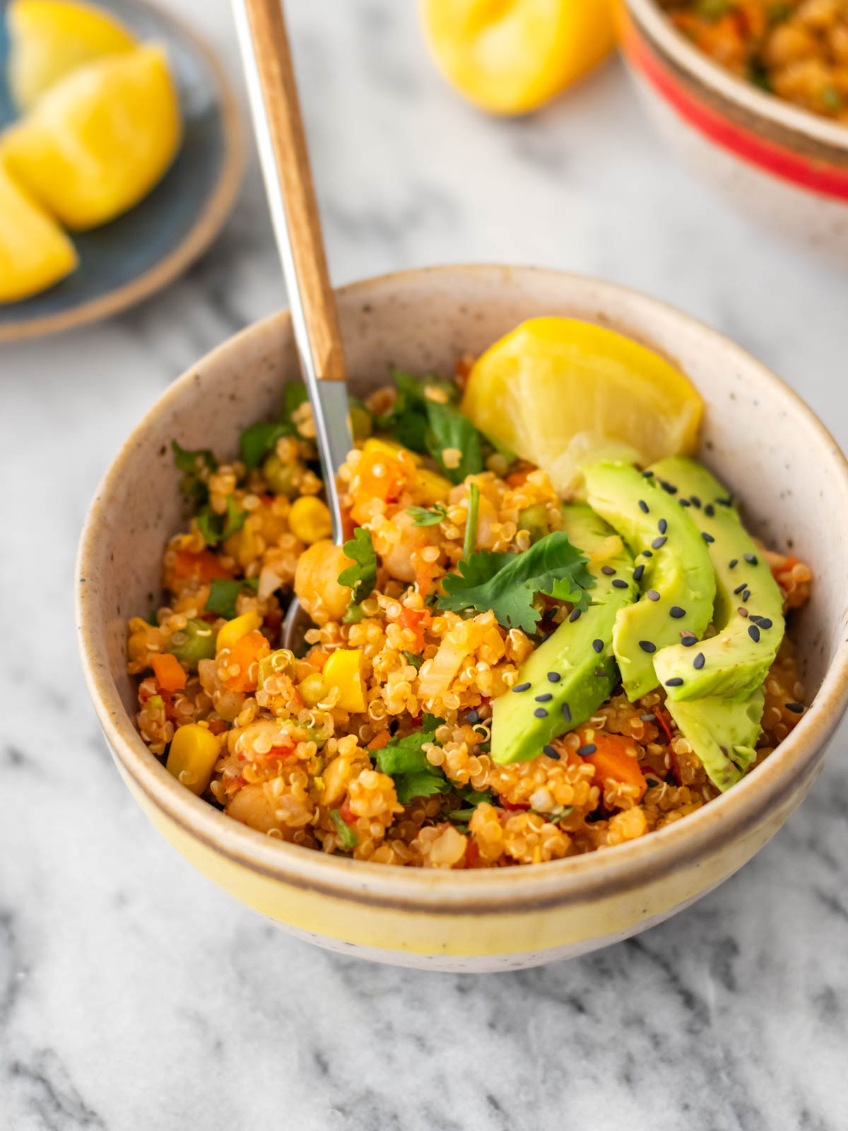 mexido de quinoa com legumes e grão-de-bico servido com fatias de abacate, sementes de gergelim e coentro fresco