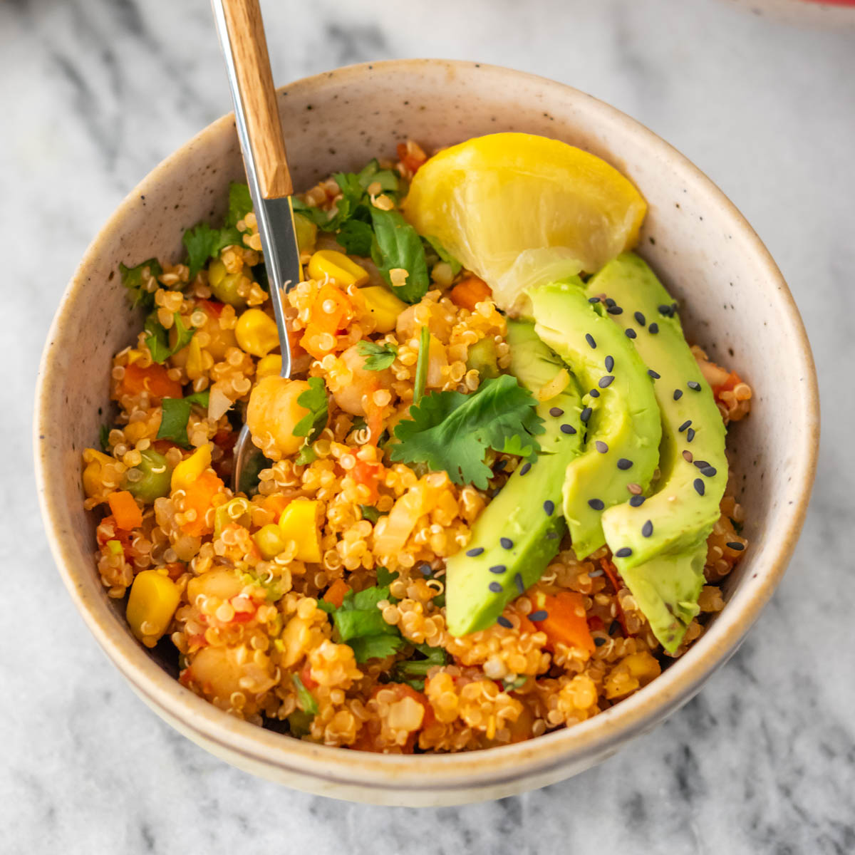 mexido de quinoa com legumes e grão-de-bico servido com fatias de abacate, sementes de gergelim e coentro fresco