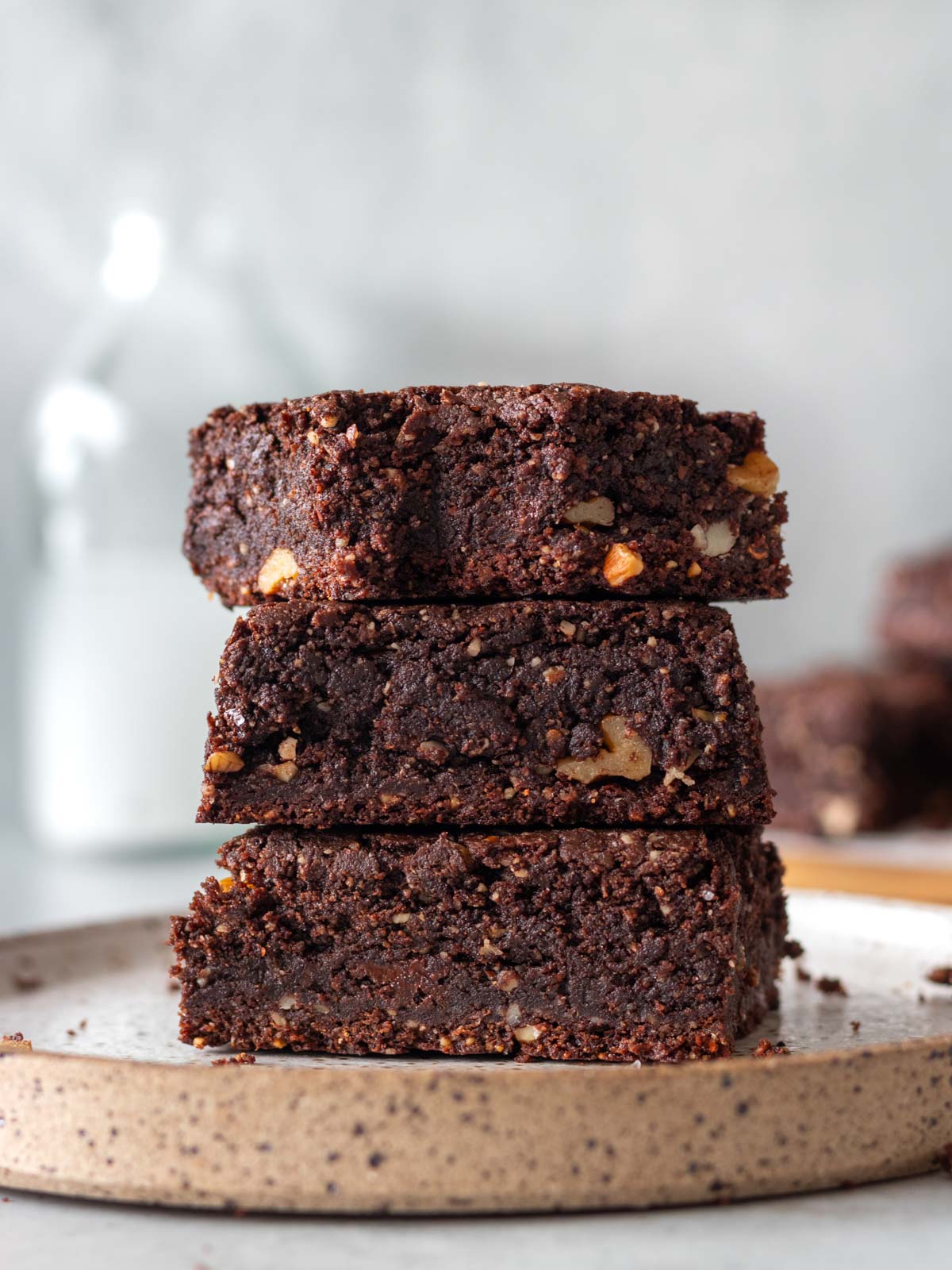 3 pedaços de brownie de amêndoas e chocolate empilhados em um prato, mostrando sua textura úmida com pedaços de nozes picadas