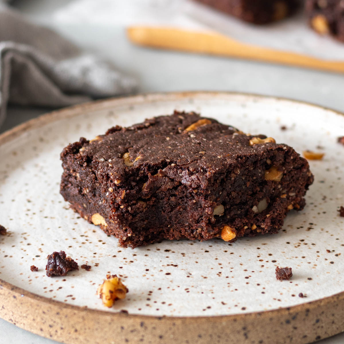 pedaço de brownie de amêndoas e chocolate mordido em cima de um prato, mostrando seu interior úmido com pedaços de nozes